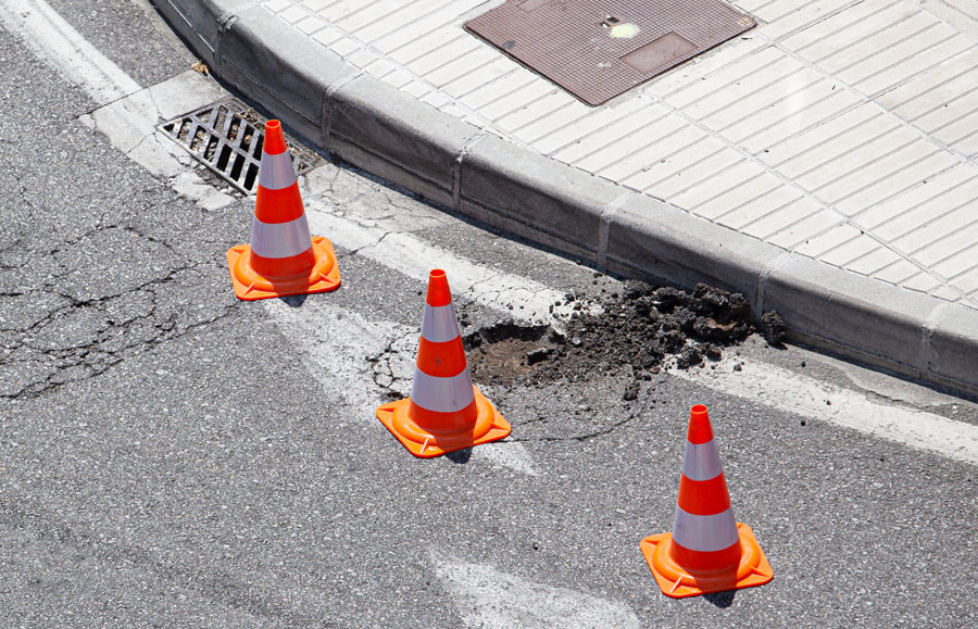 A pothole near a curbed sidewalk marked with three cones.