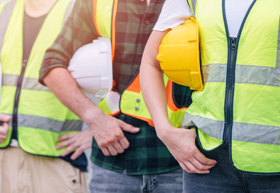 Three road crew members in hi-viz vests standing holding their hard hats.